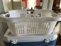 White plastic laundry basket on top of a cooler box, showing ventilation slots and integrated handle grips