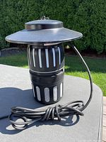 Black Dynatrap mosquito trap device shown on a table outside with coiled power cord visible.