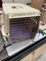 Front angle of beige Kennel Cab II pet carrier showing metal front door, built-in handle on top, and purple interior padding