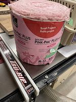 Partial roll of pink Owens Corning Pink-Pak Plus fiberglass insulation R-12 in original packaging, shown on a table.