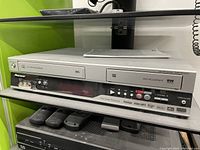 Front view of Pioneer VHS/DVD Recorder showing VHS tape slot, DVD recorder slot, front controls, and remote controls below on shelf