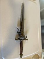 Photo of a decorative pistol dagger showing the pistol-shaped metal guard, wooden handle, and metal blade against a white background.