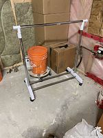 Portable chrome metal clothes rack with white plastic joints and lockable wheels. Standing on a concrete floor.