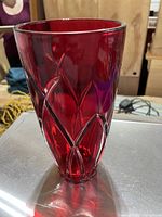 Red glass vase with faceted geometric cut pattern, photographed on a table showing full vase shape and color