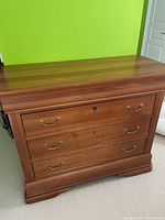Front right angle view of the solid cherry wood four-drawer dresser against a green wall