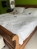 Angled view of cherry wood sleigh bed with white bird-print bedding and matching nightstands