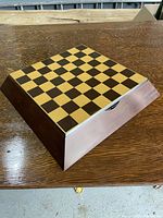 Closed view of wooden chess and checkers board showing dark and light squares arranged in an 8x8 grid on top of a wooden box with drawer feature.