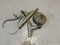 Photo showing a set of wood lathe accessories including a pair of calipers, a four-jaw chuck, and two tool rests measuring approximately 6 inch and 12 inch.