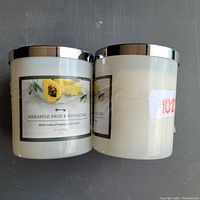 Two white jar candles with silver lids, labeled Pineapple sage & sugarcane with notes of papaya and melon.