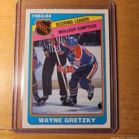 Front view of Wayne Gretzky Scoring Leader 1983-84 OPC hockey card #380 showing player in blue Edmonton Oilers uniform on ice during a faceoff.