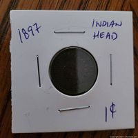Front side of 1897 Indian Head one cent coin in protective cardboard holder with handwritten text