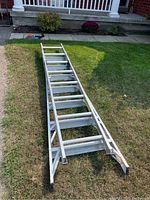 Full length shot of the aluminum extension ladder on grass showing the rungs and black rubber feet for stability.