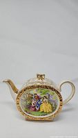 Front side view of antique James Sadler ironstone teapot showing oval hand-painted courting couples scene, gold gilding on handle and spout, and bow-shaped lid handle.