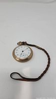 Waltham pocket watch lying flat showing dial, strap looped nearby