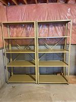 Front view of two mustard yellow steel shelving units side-by-side in a basement storage area with pink insulation on walls.