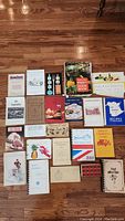 Photo showing the full collection of vintage cookbooks and recipe booklets laid out on a wooden floor.