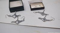 Two pairs of silver tone vintage Hoselton earrings laid flat with jewelry boxes behind.