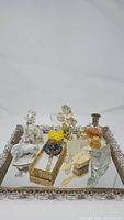 Full view of vintage decorative silver-tone framed mirrored tray with assorted vintage perfume bottles and vanity items arranged inside.