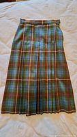 Green, brown, and blue plaid pleated skirt laid flat