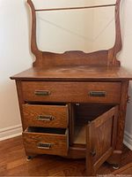 Front view of antique wooden washer stand with two upper drawers, two lower drawers, one cabinet door opened, showing interior and mounted on small wheels.