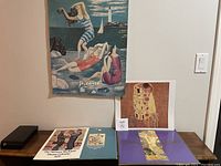 Photo showing several art prints laid out including a Picasso beach scene print, an unframed Klimt print of 'The Kiss', art calendar pages and a purple Gustav Klimt print portfolio folder.