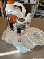 All items arranged together on a table to show contents of the lot: plastic paint palettes, flood medium container, gouache paint jar, acrylic medium bottle, acrylic paint bottles.