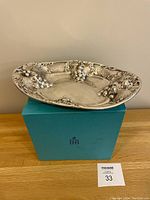 Silver plated oval tray displayed on top of turquoise box with visible grape motifs and smooth polished surface.