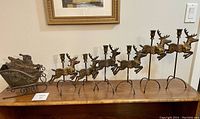 Full display of brass Santa sleigh and six reindeer candle holders arranged on wooden surface