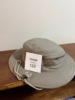 Beige canvas bucket hat with medium-wide brim and adjustable drawstring laid on a wood surface.