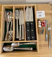 Wooden compartmentalized tray containing assorted cutlery and decorative serving utensils.