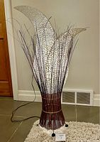Full view of the floor lamp showing its woven bamboo base, black ball feet, and three leaf-shaped translucent shades with patterned design.