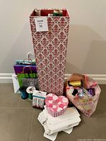 Tall gift bag with red floral pattern, assorted smaller gift bags, large rolled wrapping paper, small gift boxes, and curling ribbon spools bundled in bags