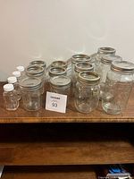 Fifteen glass jars and bottles arranged on a wooden shelf; various sizes of mason jars and small glass bottles with white plastic caps.