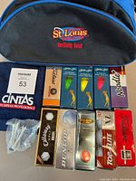 Photo shows the St. Louis branded shoe bag, multiple new boxes of golf balls from brands Titleist, Callaway, Dunlop, Top Flite, and Noodle+, a white Cintas golf towel, and a small bag of white golf tees.