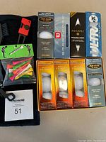 Photo showing all items included in lot: boxed golf balls from Wilson, Maxfli, Pinnacle, and Tour XL, colored golf tees in bag, and black golf towel with clip.