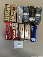 Ten boxes of different brands of golf balls arranged on a gray surface, each box unopened and new in box.