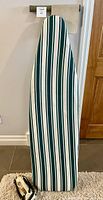 Full view of large ironing board with green, white, and blue striped padded cover.
