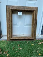 Photo of a large solid wood picture frame with textured Italian sand finish, shown against a white door background and grass beneath.