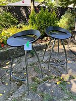 Photo showing two modern black bentwood bar stools with metal tubular legs on stone ground outside.