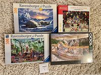 Photo showing four puzzle boxes arranged on carpet: two Ravensburger 500-piece puzzles with seals and greenhouse scenes, one 300-piece Artpuzzle 'Imaginary City' puzzle, and one 1000-piece Barcelona park puzzle.