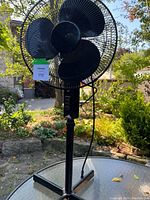 Full view of the black 16-inch oscillating fan standing on a flat surface outdoors with all parts visible including blades and protective grill.