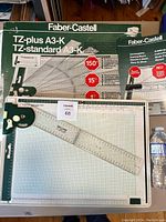 Faber-Castell TZ-plus A3-K technical drawing board in green with pivoting ruler and protractor attached, showing all measurement markings and packaging box in background.
