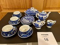 Full set arranged on black surface showing cups, saucers, plates, teapot, sugar bowl, creamer, and covered serving bowl with blue and white traditional pattern.