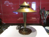 Art Deco two-tiered metal table lamp with two-tiered pagoda-shaped shade on white fabric background showing full lamp profile with cord and switch