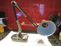 Side angle view of articulating lamp on heavy base, showing reflective inside of lamp head and the adjustable arms.