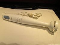 Full view of white Braun immersion blender showing power button, cord, and blending shaft.