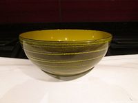 Front and side view of yellow and dark green enamel bowl with yellow ring pattern showing exterior surface.