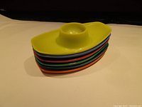 Stacked view of 6 colorful plastic egg cups showing oval bases and cup holders, stacked in the order yellow, blue, teal, green, orange, red.