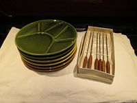 Stack of six divided fondue plates in green, brown, and mustard yellow with set of six fondue forks in original box.