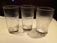 Three drinking glasses on table, including one wavy textured Iittala Aslak glass and two less defined glasses